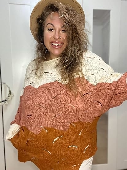 Smiling person wearing a hat and a cream, pink, and orange layered knit sweater.
