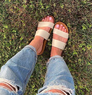 reviewer photo of a person wearing ripped jeans with tan sandals standing on grass
