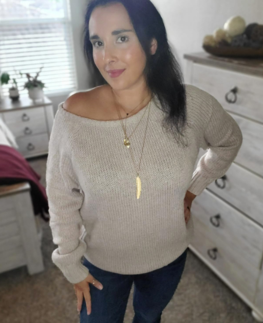 Reviewer modeling an off-the-shoulder sweater and long necklace in a bedroom setting