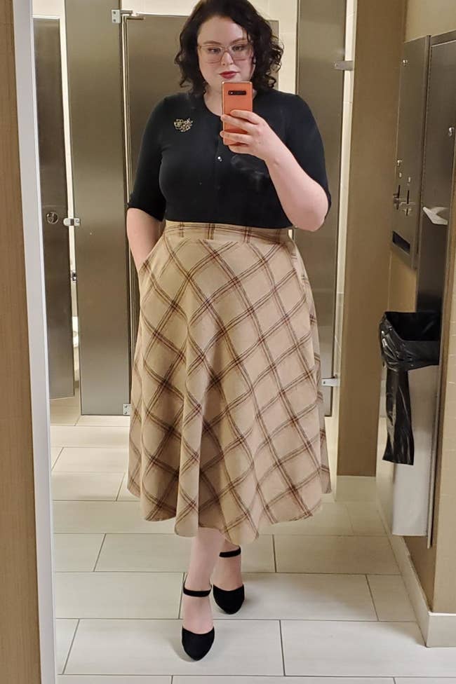 a reviewer mirror selfie of them wearing the skirt in tan with a black shirt tucked in 