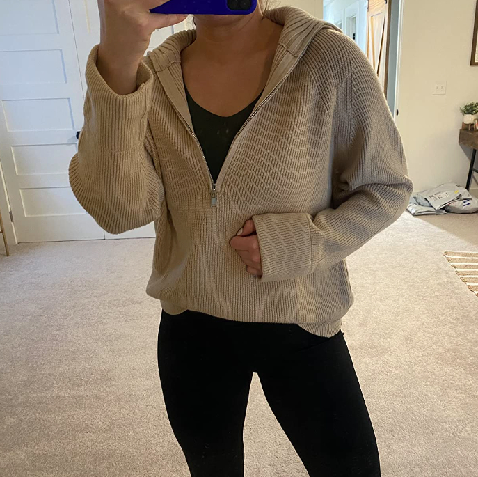 A person takes a mirror selfie wearing a ribbed zip-up hoodie layered over a dark shirt, paired with black leggings