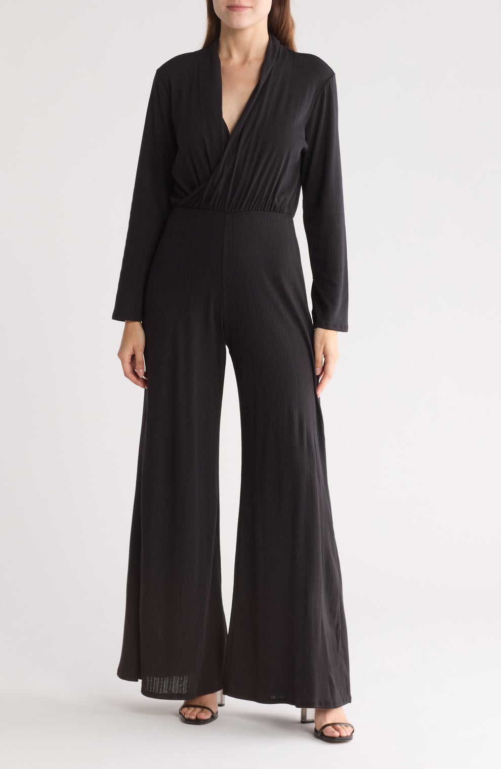 A person wearing a stylish black jumpsuit with long sleeves and wide-leg pants, standing against a plain background