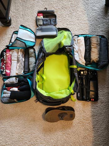 Travel backpack with neatly organized compartments, including clothes, toiletries, electronics, and sandals, showcasing efficient packing for a trip